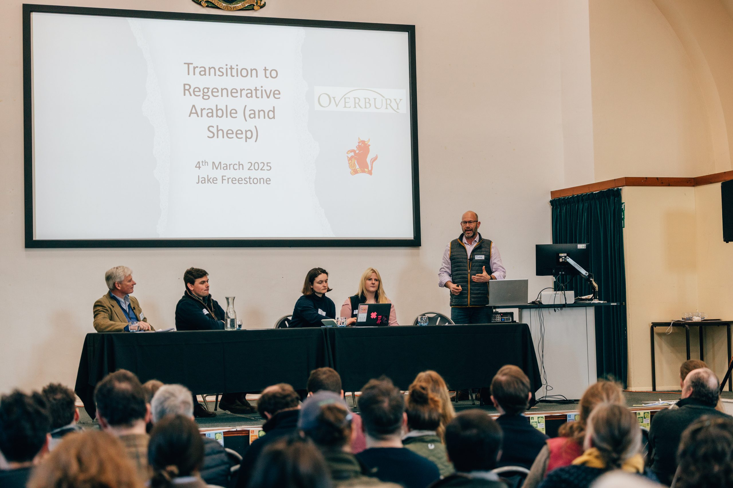 Image shows the Cotswolds Regenerative Agriculture Conference 2025 panel members, speaking to a full audience.