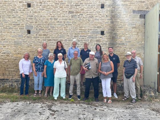 Image shows a group of smiling people standing in front of a stone barn.